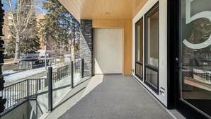 A modern building with a balcony, large windows, and a stone facade. - Onyx Escape | Lux 2 Bed | Garage | Min to DT (Calgary)