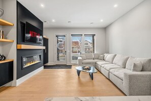 Ein modernes Wohnzimmer mit Kamin, Ecksofa, Wand-Fernseher und großem Fenster.