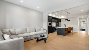 A modern living room with a sofa, a coffee table, and a kitchen area with a dining table and chairs. - Onyx Escape | Lux 2 Bed | Garage | Min to DT (Calgary)