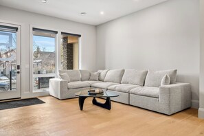 Ein modernes Wohnzimmer mit einem Ecksofa, einem Glastisch und Blick durch große Glasschwingtüren.