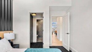 Et hotelværelse med en seng, et natbord, en lampe, et badeværelse med bruser og udsigt ud.