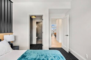 Ein Hotelzimmer mit Bett, Nachttisch, Lampe, Badezimmer mit Dusche und Blick ins Freie.
