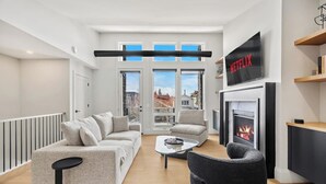 En moderne stue med sofa, lænestol, sofabord, pejs, tv og store vinduer.