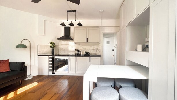 Una cucina moderna con mobili bianchi, forno integrato e zona pranzo con tavolo bianco e sgabelli grigi.
