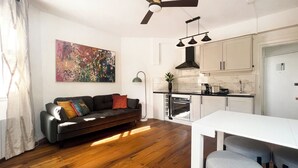 Un soggiorno moderno con divano, tavolo da pranzo, angolo cottura con pensili ed elettrodomestici, e una ventola a soffitto.