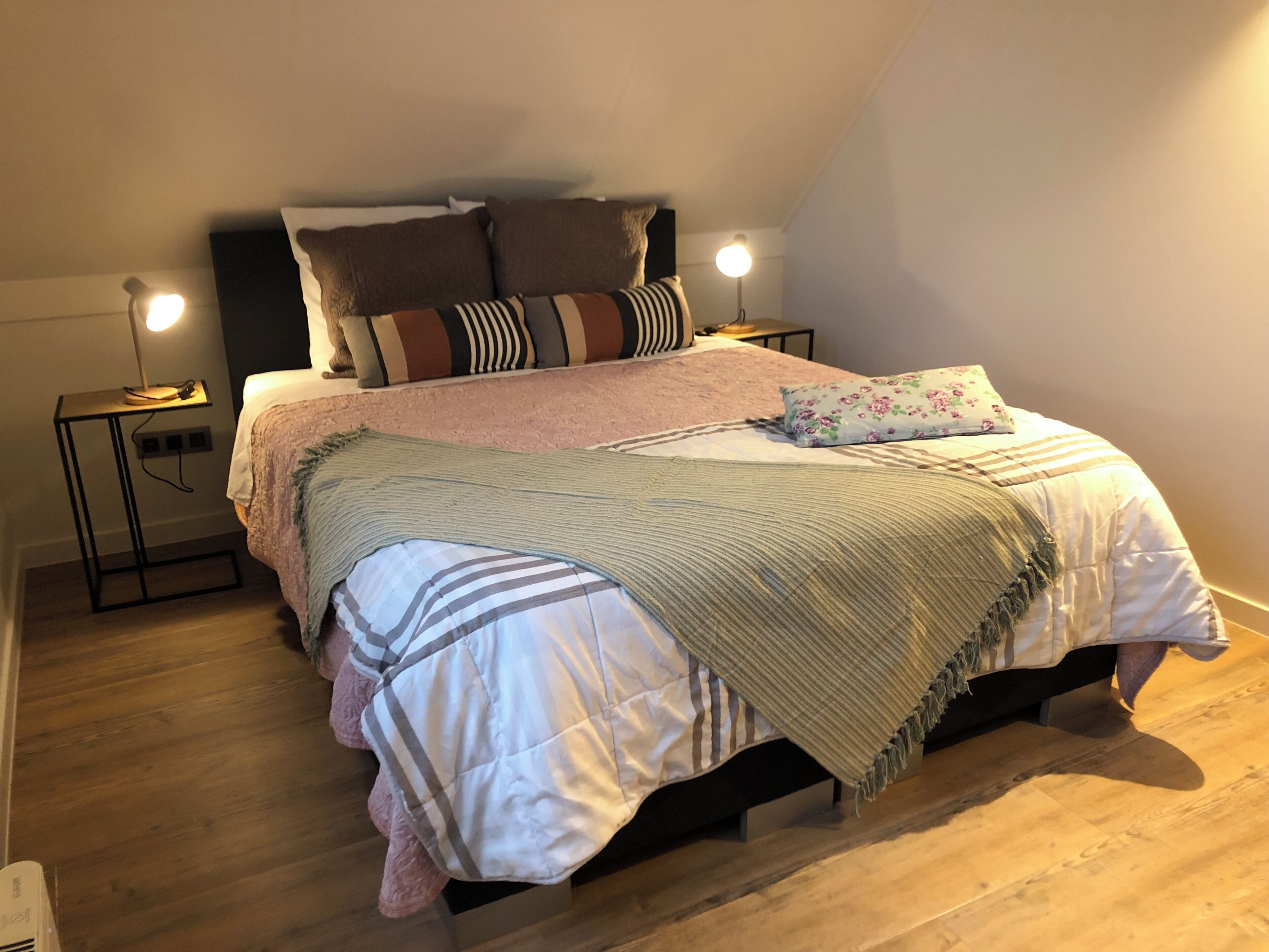 Une chambre à coucher avec un lit, deux tables de chevet, une lampe et un plancher en bois.