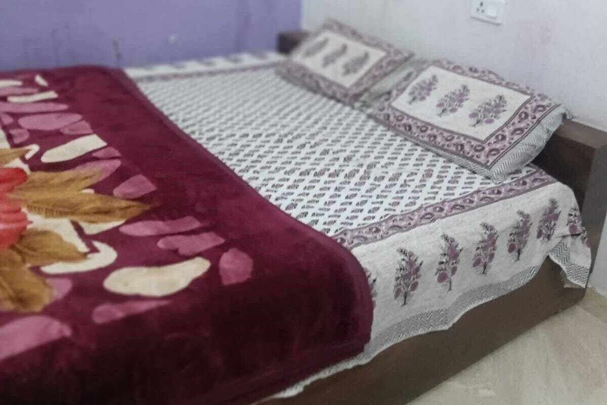 Ein kleines Zimmer mit einem Einzelbett, einer violetten Wand, einer gemusterten Tagesdecke und einem weißen Kissen mit floralem Muster.
