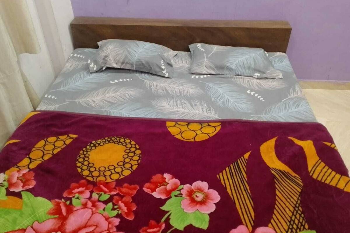 Ein Bett mit einem gemusterten Überwurf und Kissen, einem Holzkopfteil und einer violetten Wand.