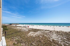 Blick auf einen Strand mit sandigem Ufer, einem Steg und einem wolkenlosen, blauen Himmel.