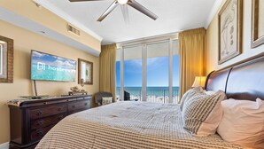 Une chambre d’hôtel équipée d’un lit, d’une télévision, d’une commode et d’un balcon avec vue sur l’océan.