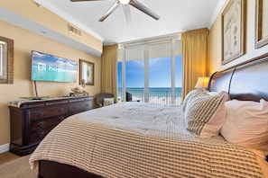 Ein Hotelzimmer mit Bett, Fernseher, Kommode und Balkon mit Meerblick.