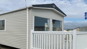 A mobile home with a white exterior, a front deck, and a large window. - Greenacres Holiday Park - Holiday Accommodation 15761 (Porthmadog)