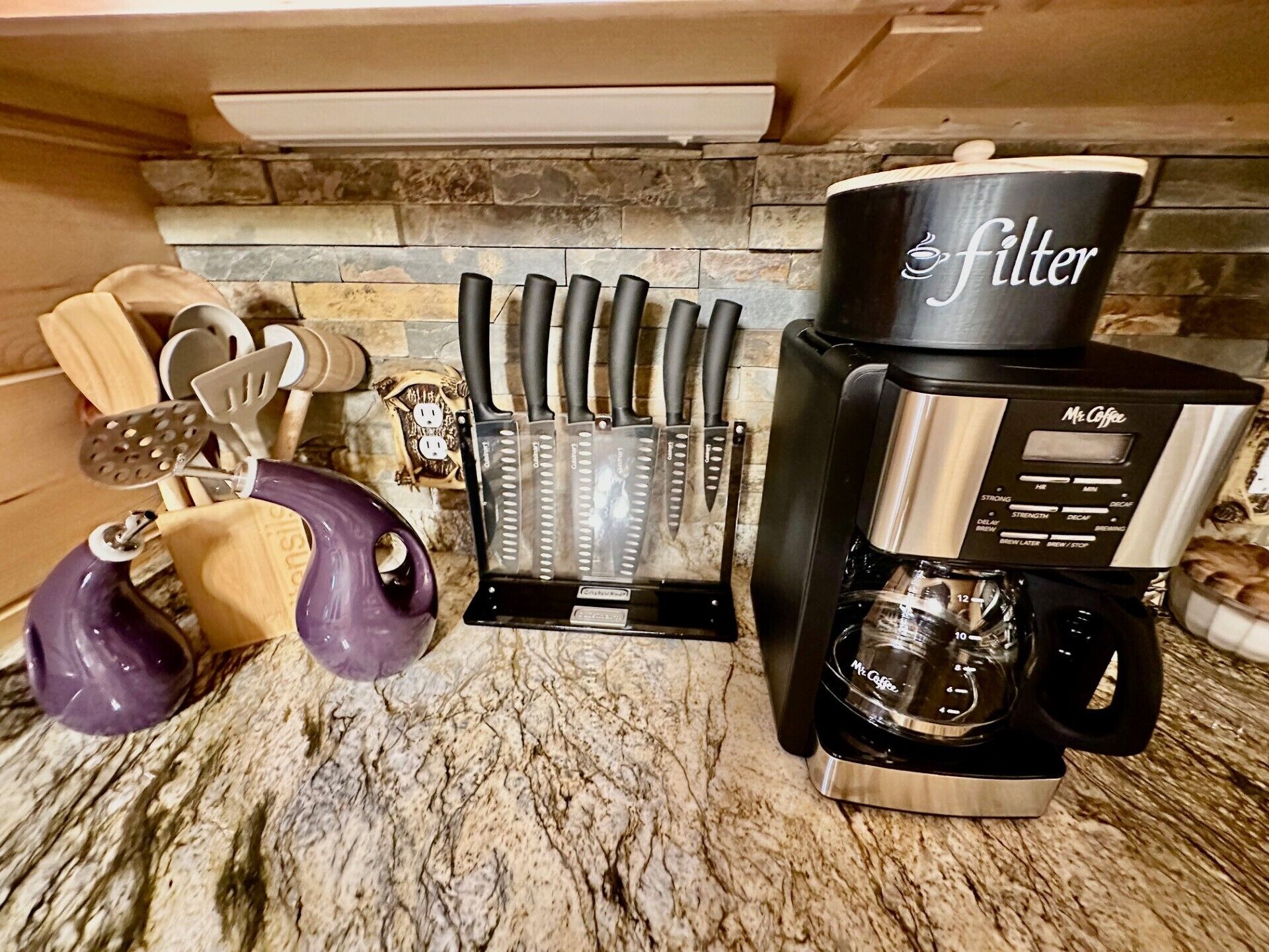 Een keukentafel met een koffiezetapparaat, een messenblok en een paarse mok.