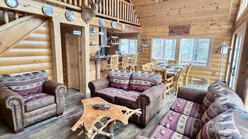 Ein rustikaler Innenraum einer Blockhütte mit Essbereich, zwei Sofas, einem Holztisch und einer Küchenzeile.