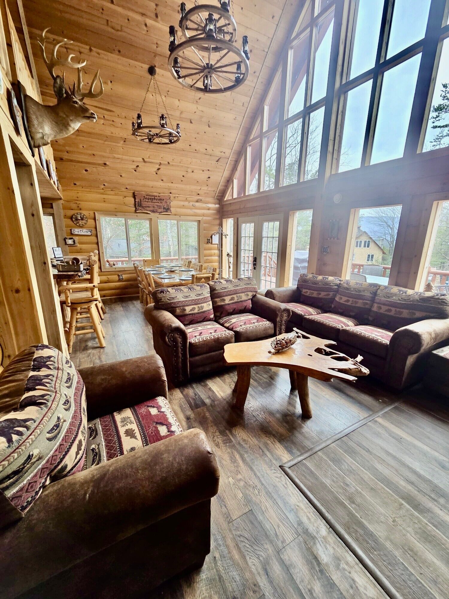 A log cabin interior with a large dining table, sofas, and a wooden coffee table.