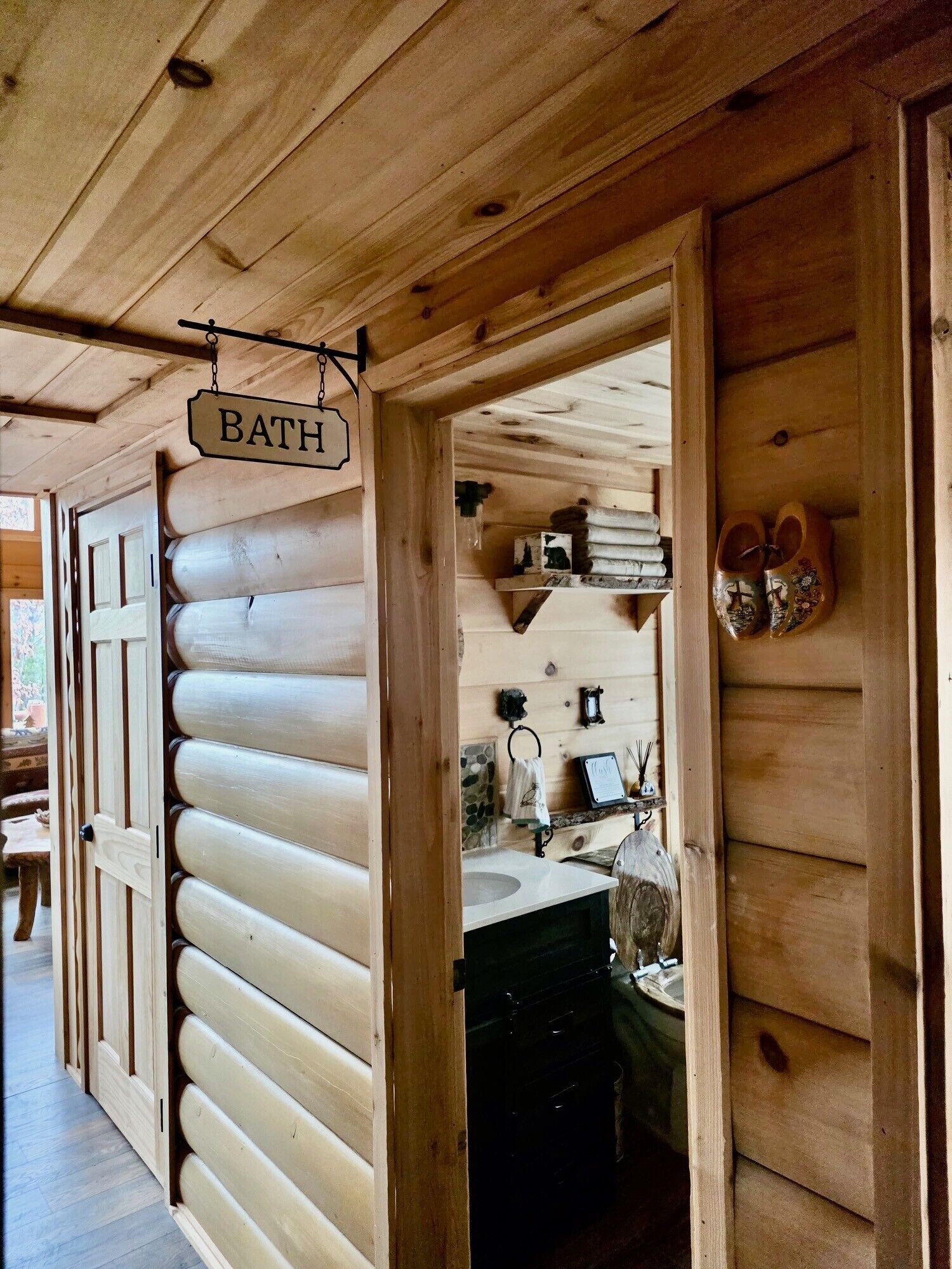 En stuga med träinredning, där man tydligt kan se badrummet med badkar, handfat och en hängande skylt med texten ”badrum”.
