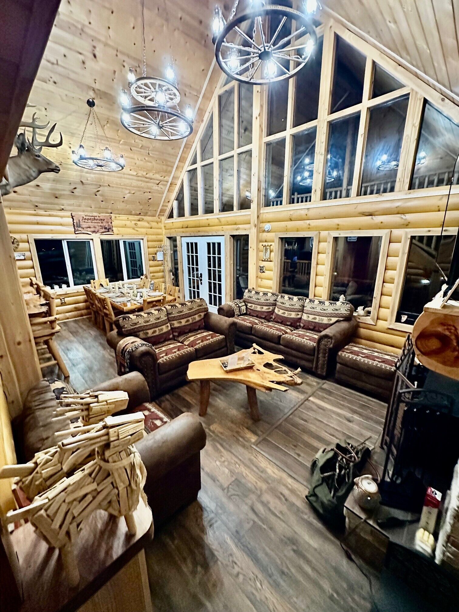 A log cabin interior with a large seating area, wooden walls, and multiple windows.