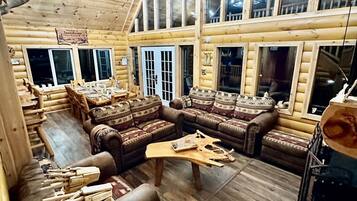 A log cabin interior with a large seating area, wooden walls, and multiple windows.