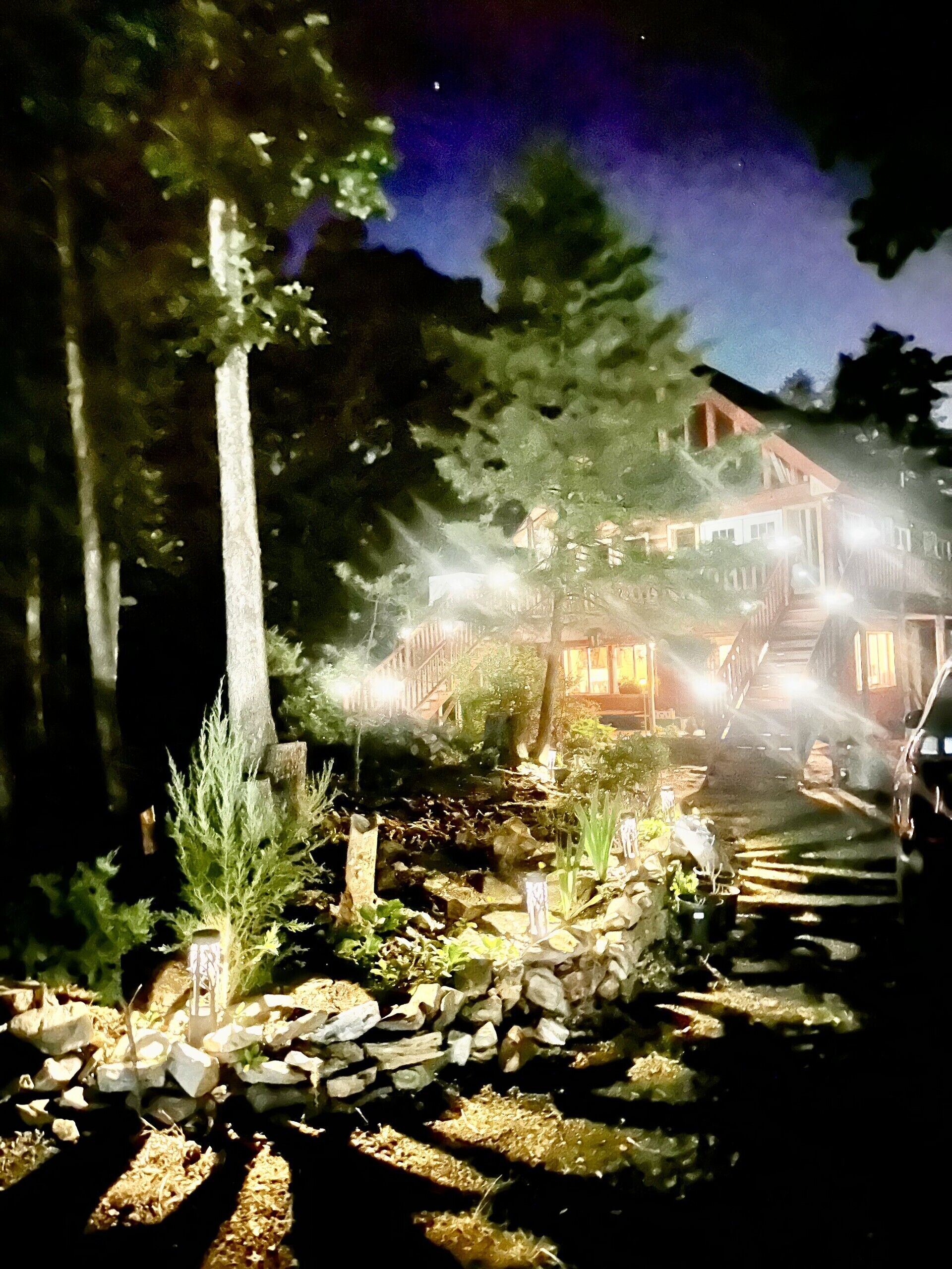 Ein Nachtblick auf ein Haus mit einem steinernen Weg, der zum Eingang führt, umgeben von Bäumen und beleuchtet durch Außenlichter.