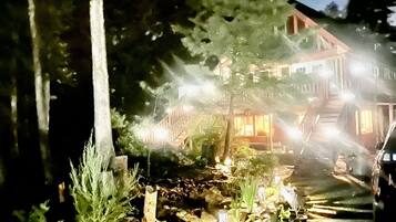 Ein Nachtblick auf ein Haus mit einem steinernen Weg, der zum Eingang führt, umgeben von Bäumen und beleuchtet durch Außenlichter.