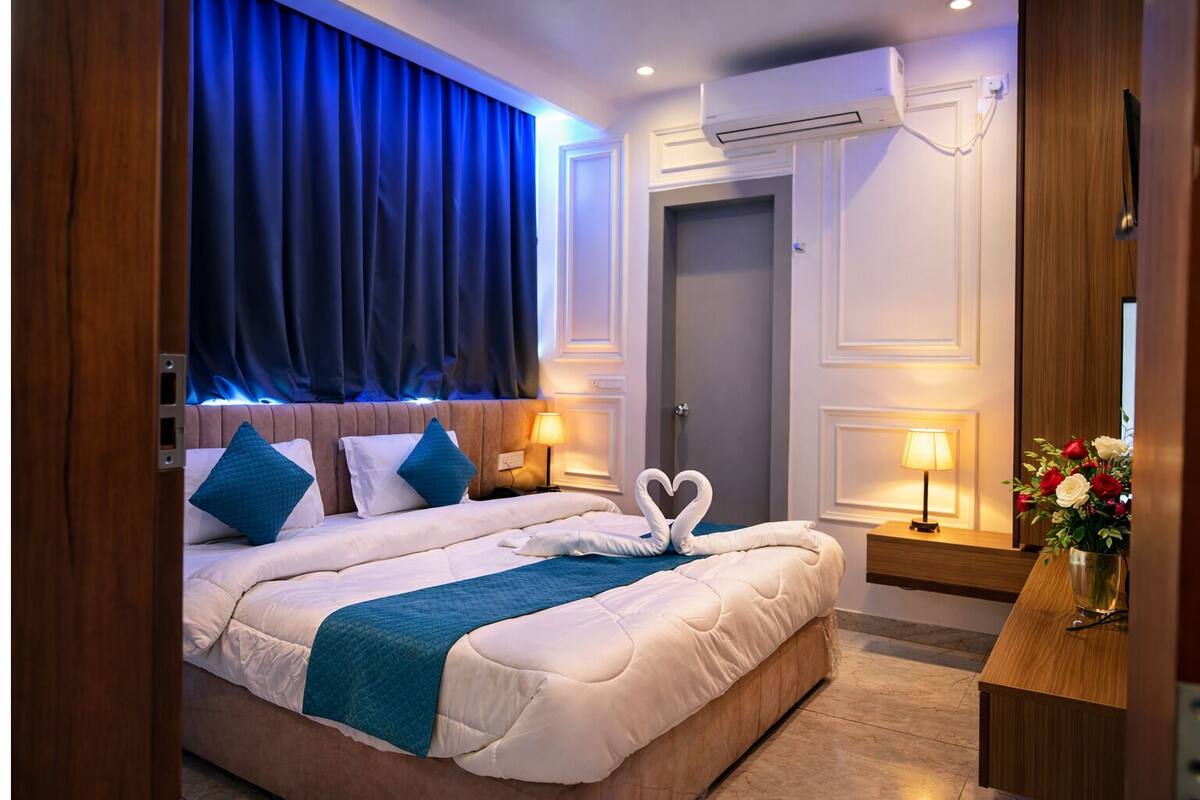 A hotel room with a bed, a desk, an air conditioning unit, and a door.