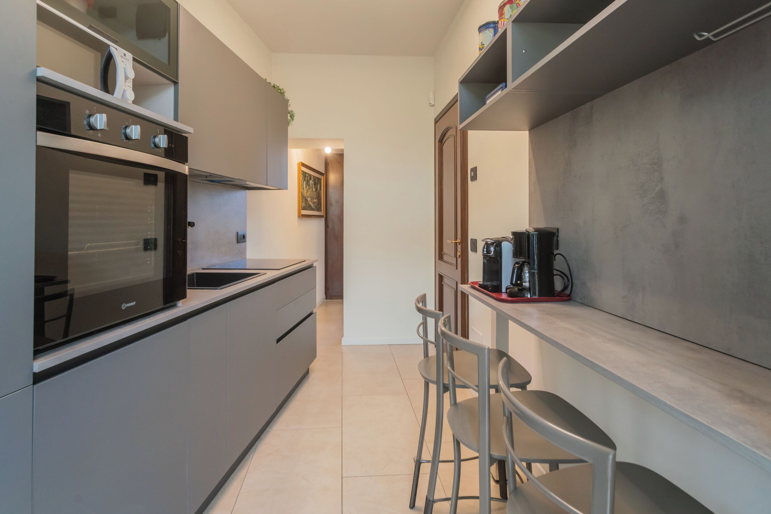 A modern kitchen with a built-in oven, a coffee machine, and bar stools.