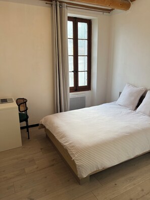 Ein Schlafzimmer mit einem Bett, einem Sessel, einem Schreibtisch und einem fenster mit Vorhängen.