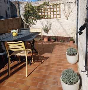 Eine Terrasse mit Tisch und Stühlen, Kübelpflanzen und einer Spalier an einer strukturierten Wand.