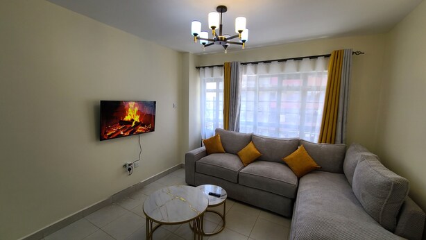 Uma sala de estar com sofá, mesa de centro, TV fixada na parede e luminária no teto.