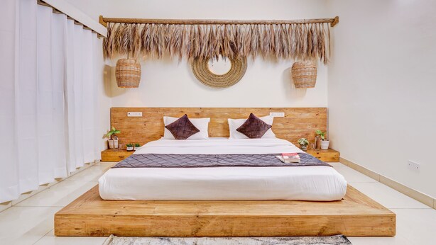 Ein Schlafzimmer mit einem Bettgestell aus Holz, weißer Bettwäsche, zwei Zierkissen, einem gewebten Wandbehang und zwei Wandkörben.