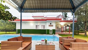 Ein überdachter Außenbereich mit Korbmöbeln, einem Pool und einem Gebäude mit roter und weißer Fassade.