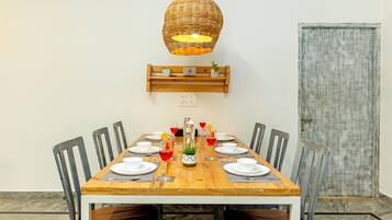 A dining table with chairs, a hanging light fixture, a wall-mounted shelf with plants, and a door.