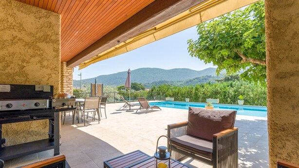 Une terrasse extérieure équipée d’un barbecue, de sièges et offrant une vue sur une piscine et des montagnes.