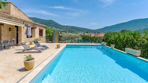 Une piscine dotée de chaises longues et d’un espace patio, le tout entouré de verdure et de collines.
