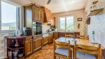 A kitchen with wooden cabinets, a dining table with chairs, a ceiling fan, and a window with a view of the outdoors.