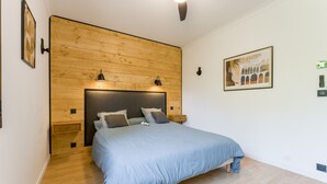 Une chambre à coucher avec une tête de lit en bois, un lit recouvert d’une couverture bleue, une table de chevet et une lampe fixée au mur.