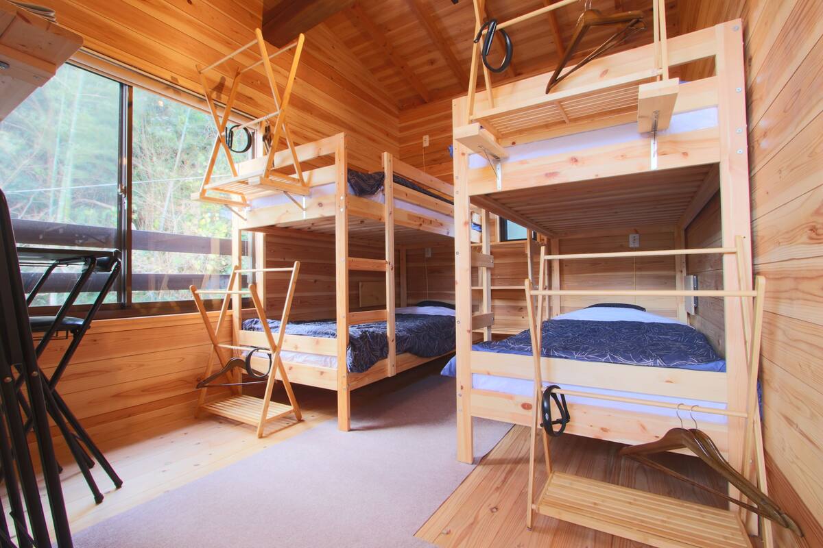 A cabin with three bunk beds, a wooden interior, and a window overlooking a forest.