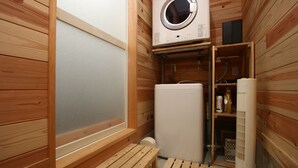 A sauna room with wooden walls, a bench, a washing machine, and a heater. - Bungee Inn (Minamiizu)