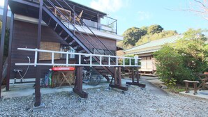 A building with a staircase, a bicycle, and a gravel path. - Bungee Inn (Minamiizu)