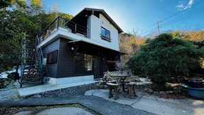 A modern two-story house with a balcony, a stone fireplace, and a small outdoor seating area. - Bungee Inn (Minamiizu)