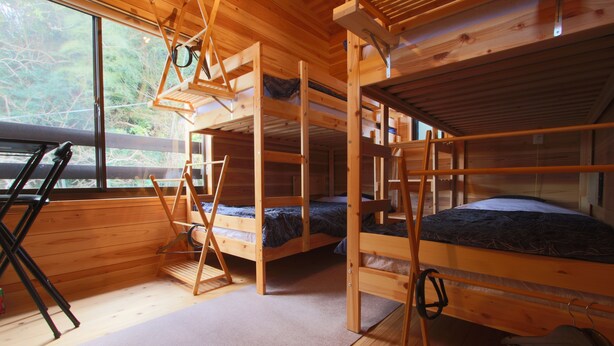 A cabin with three bunk beds, a wooden interior, and a window overlooking greenery. - Bungee Inn (Minamiizu)