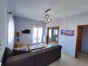 A living room with a sofa, a coffee table, a TV mounted on the wall, and a painting on the wall. - Overlooking the Tower by RentalsPro - Nea Fokea Halkidiki (Nea Fokea)