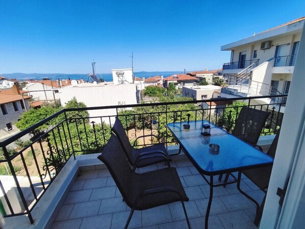A balcony with a table and chairs, a view of the sea, and surrounding buildings. - Overlooking the Tower by RentalsPro - Nea Fokea Halkidiki (Nea Fokea)