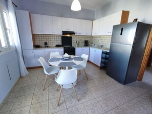 A kitchen with white cabinets, a black stove, a stainless steel refrigerator, and a round table with four chairs. - Overlooking the Tower by RentalsPro - Nea Fokea Halkidiki (Nea Fokea)