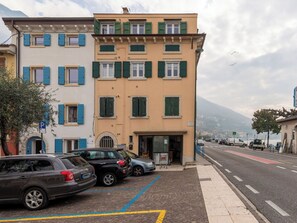Ein mehrgeschossiges Gebäude mit Eingang im Erdgeschoss, parkenden Autos und Blick auf die Straße.
