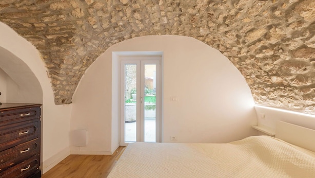 A bedroom with a stone ceiling, a wooden dresser, a bed, and a door leading outside. - Nice apartment for 5 guests with A/C, WIFI and patio (Magugnano)