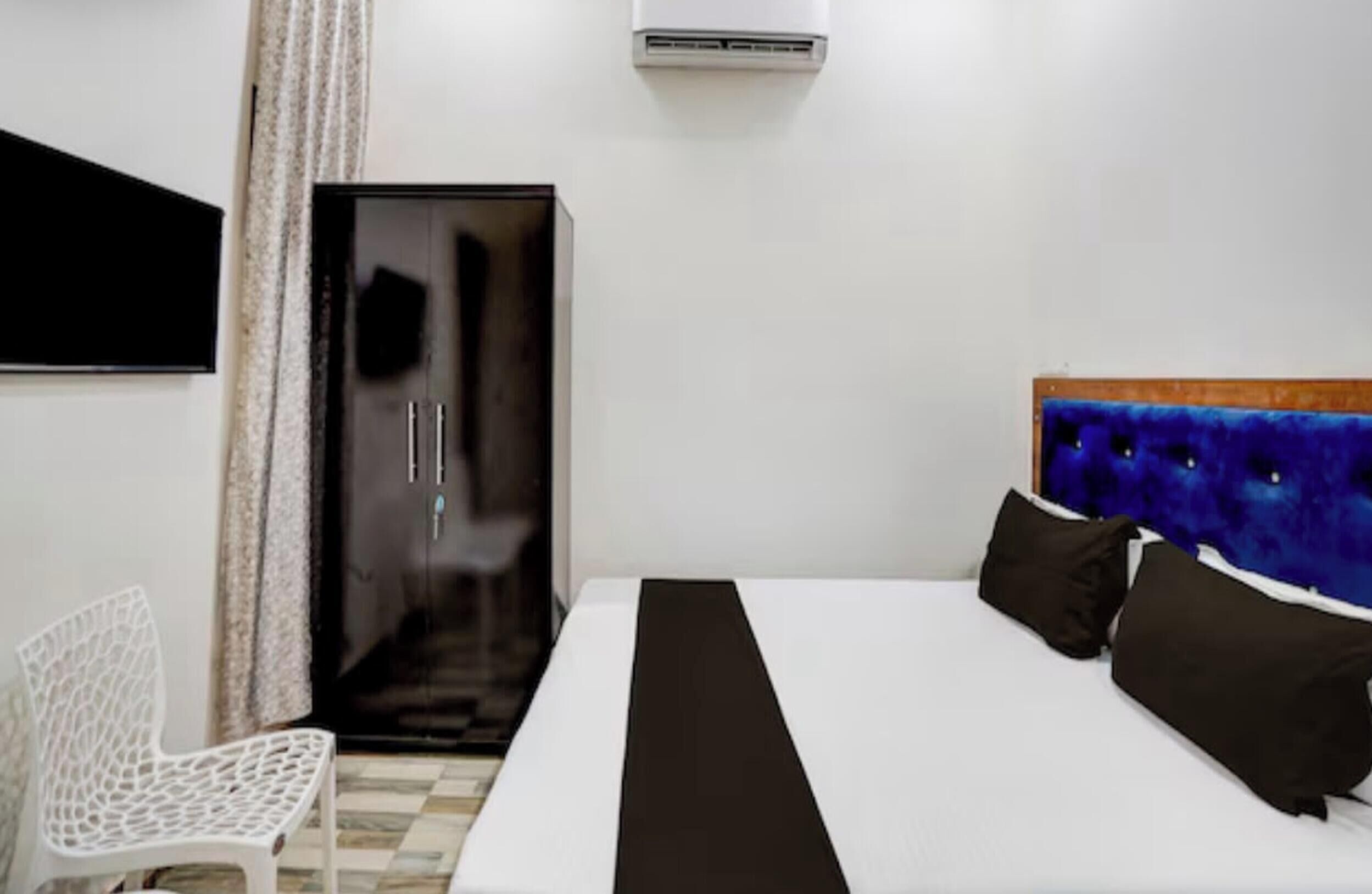A hotel room with a bed, a chair, a wardrobe, and an air conditioning unit.