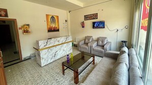 A living room with a marble reception desk, a sofa, a coffee table, and a TV mounted on the wall. - Hotel Pilgrrim (Varanasi)