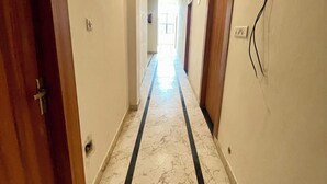 A corridor with marble flooring, wooden doors, and a light fixture on the wall. - Hotel Pilgrrim (Varanasi)