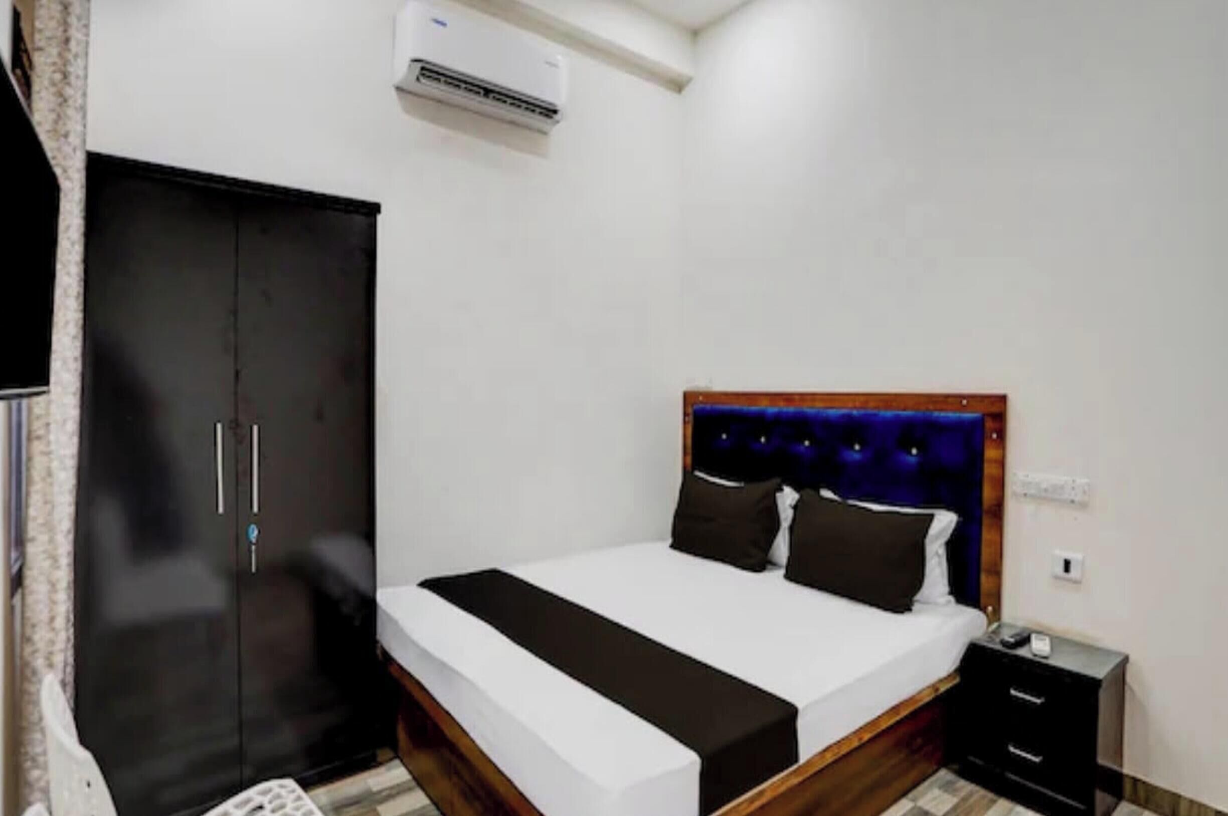 A bedroom with a bed, a wardrobe, a nightstand, and an air conditioning unit.